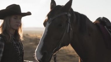 Kovboy şapkalı okşayarak ve bir at sarılma uzun saçlı Genç sarışın kız