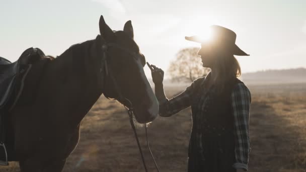 Молода блондинка в ковбойському капелюсі погладжує і обіймає коня і насолоджується природою — стокове відео