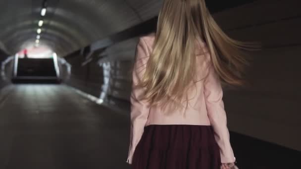 Charmante jonge meisje loopt door de tunnel in roze jas bij zonsondergang — Stockvideo
