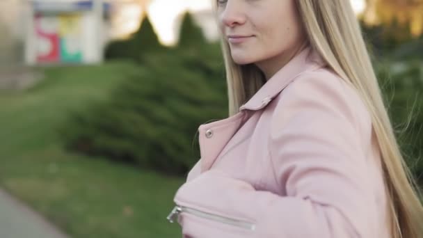 Блондинка выходит на улицу. Сексуальная женщина в розовой куртке в городе в замедленной съемке — стоковое видео
