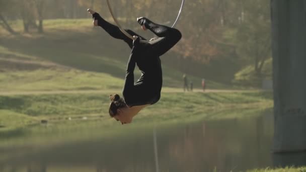 Mujer gimnasia aérea realiza acrobacias truco en aro aéreo. Morena flexible — Vídeo de stock