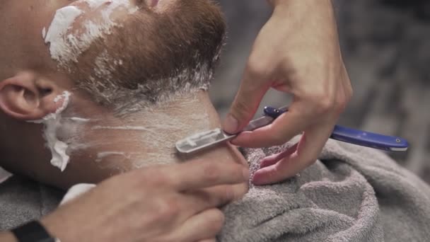 Парикмахер бреет бородатого мужчину с бритвой в мужском салоне. Закрыть бритье — стоковое видео