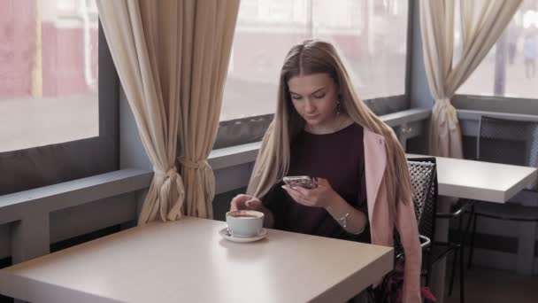 Roztomilá dívka, zasílání zpráv a pití kávy v kavárně města. Žena pití kávy — Stock video
