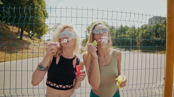 Cheerful hipster girls in sunglasses having fun making bubbles outdoors — Stock Video
