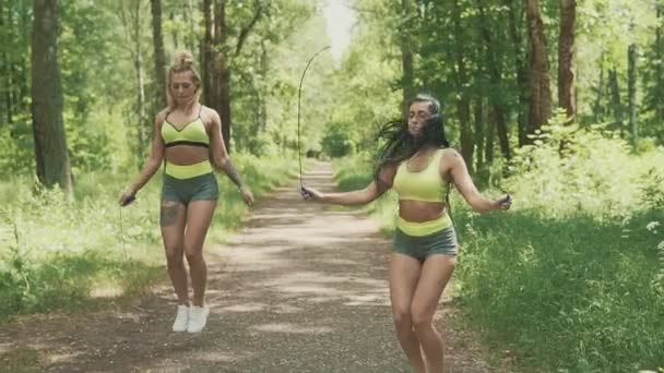 Dos mujeres jóvenes saltando la cuerda en el parque en cámara lenta. concepto de estilo de vida saludable — Vídeos de Stock