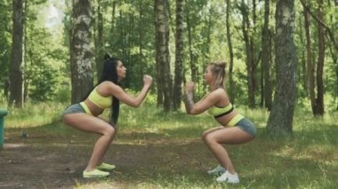 İki genç kadın parkta çömelme. Fitness modelleri dövme egzersiz ile açık