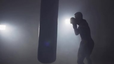 Boksör sayısı kum torbası koyu spor salonunda. Genç adam kapalı eğitim