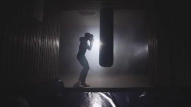 Boksör sayısı kum torbası koyu spor salonunda. Genç adam kapalı eğitim