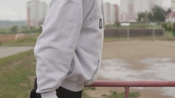 Jovem com capuz fazendo flexões em barras horizontais paralelas durante o treino — Vídeo de Stock