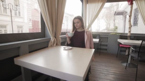 Χαριτωμένο κορίτσι πίνοντας τον καφέ στην καφετέρια κατά τη διάρκεια διαλείμματος. Νεαρή γυναίκα με το καφέ — Αρχείο Βίντεο