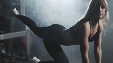 Sexy blonde woman training in sport center. Girl doing kick backs on bench