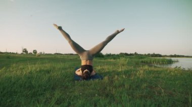 Esmer kadın pratik yoga Park. Yoga yaparken kız yeşil çimenlerin üzerinde hareket eder.