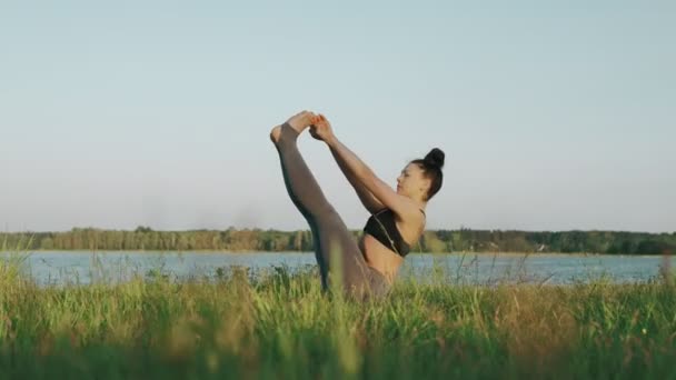 Mooie vrouw beoefenen van yoga in de ochtend. Meisje doen yoga beweegt op het groene gras — Stockvideo