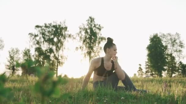 Mujer morena practicando yoga en el parque. Chica haciendo yoga se mueve sobre hierba verde — Vídeos de Stock