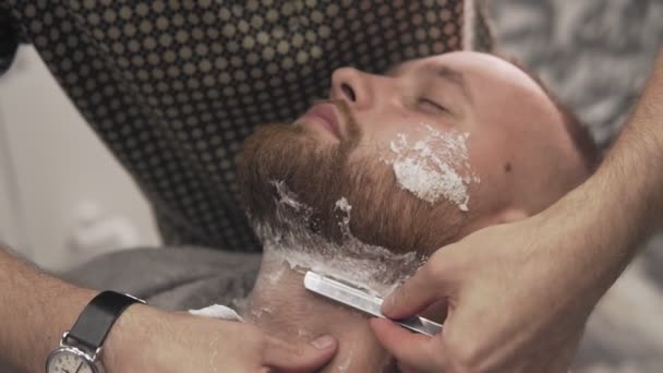 Peluquero afeitado hombre barbudo con navaja de afeitar recta en el salón. concepto de cuidado de la piel masculina — Vídeo de stock