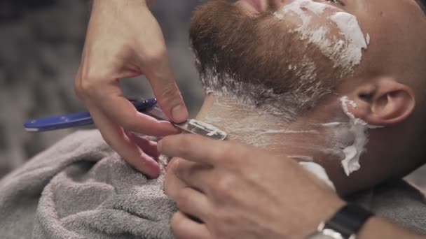 Перукарська гоління бородатий чоловік з прямою бритвою в перукарні. Чоловічий догляд за шкірою — стокове відео