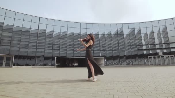 Красивая женщина в черном платье играет на скрипке возле стеклянного здания. Концепция искусства — стоковое видео