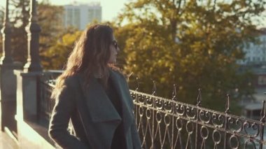 Güneş gözlüklü şirin genç kız ceket ve gülümsüyor sonbahar şehirde size yürür