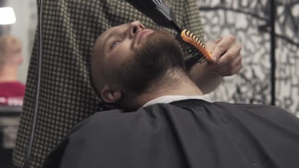 Barbero barba de afeitar con maquinilla de afeitar eléctrica en salón masculino. Afeitarse hombre barbudo — Vídeos de Stock