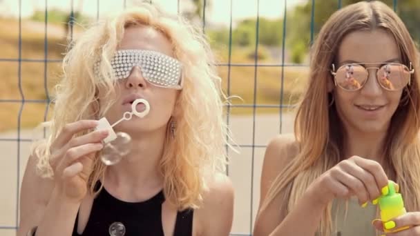Cheerful hipster girls in sunglasses having fun making bubbles outdoors — Stock Video