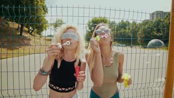 Beautiful hipster girls in sunglasses having fun making bubbles outdoors — Stock Video