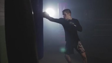 Boks çantası ile Kickboxer eğitimi. Dumanlı stüdyoda Muay Thai Fighter delme
