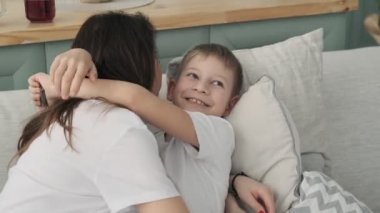 Mutlu genç aile evde birlikte vakit geçirmek. Oğul sarılmak anne yavaş hareket. Oturma odasında gömlek ve kot anne ve oğul