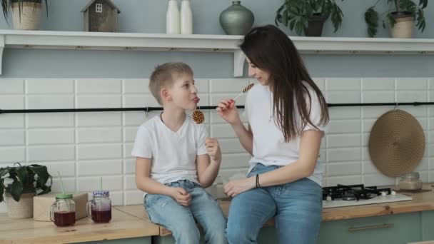 若い母親と息子は台所でキャンディーを楽しんでいます 幸せなお母さん過ごす時間とともに息子座って上のテーブルの上にスローモーション — ストック動画