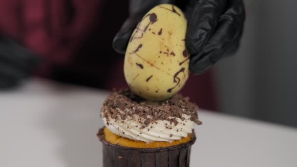 糖果师用巧克力蛋做纸杯蛋糕 手套双手的特写镜头 以慢动作用巧克力蛋装饰杯形蛋糕 家庭面包店概念 一步一步 — 图库视频影像