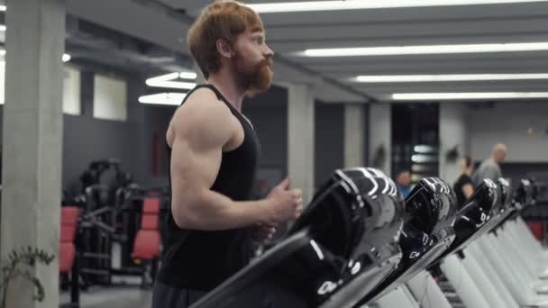 Joven pelirroja atlético hombre haciendo ejercicio y corriendo en la cinta de correr en el gimnasio deportivo — Vídeos de Stock