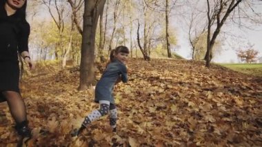 Anne ve kızı oynarken ve sonbahar yaprakları trowing. Aile yavaş çekimde sonbahar parkında eğleniyor. Mutlu aile konsepti. Tam uzunlukta çekim