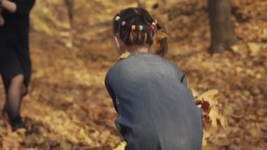 Mutlu anne ve küçük kızı sonbahar parkında eğleniyor. Annem yavaş çekimde kızıyla oynuyor. Orta atış