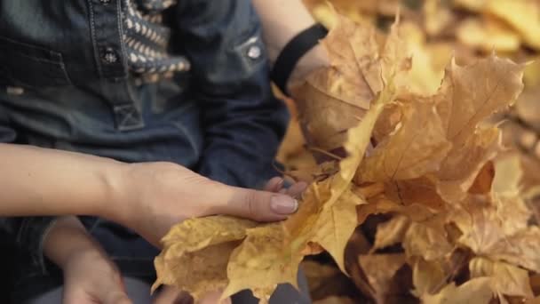 Gros plan de maman embrassant sa fille dans le parc d'automne. Mère et fille jouent avec les feuilles d'automne. La famille s'amuse au ralenti. Concept de famille heureuse 