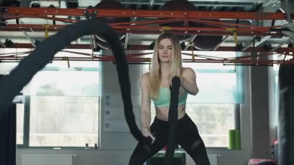 Athletic female exercises with battle ropes in gym. Fitness workout of blonde woman in slow motion. Medium shot — Stock Footage Athletic Female Exercises Battle Ropes Gym Fitness Workout Blonde Woman Royalty Free Stock Footage
