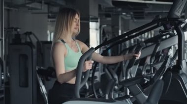 Atletik sarışın kadın spor salonunda step makinesi üzerinde çalışıyor. Fitness kulübünde genç ince kadın. Orta atış