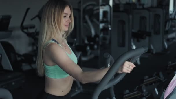 年轻女子在椭圆教练上做有氧运动时 适合在健身房训练的金发女人 — 图库视频影像