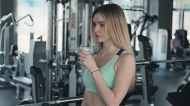 Güzel kadın eğitimden sonra camdan su içiyor. Yavaş çekimde tatlı suyun tadını çıkaran seksi sarışının portresi. Orta atış