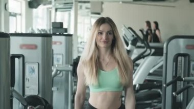 Fitness stüdyosunda yürüyen beyaz beyaz güzel kadının ön görünümü. Fitness kulübüne giren genç sarışın kadın. Orta atış. İzleme kamerası