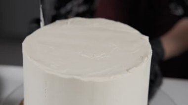 Baker krem şanti ile kek yumuşatma kapatın. Siyah eldivenli kadın eli sünger kek üzerine krem şanti beyaz krema serpişiyor. Baker spatula kullanarak krema ile pasta hazırlama.