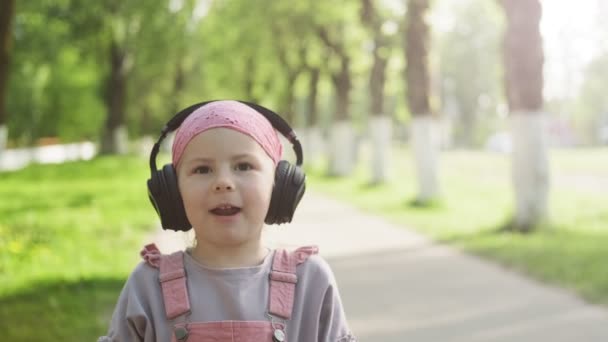 Lycklig Liten Flicka Bär Trådlösa Hörlurar Lyssna Musik Titta Kamera — Stockvideo