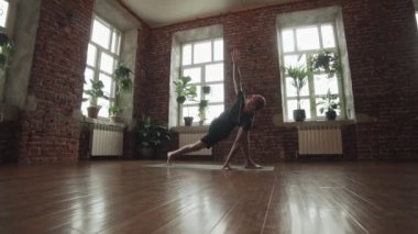 Çekici adam yavaş çekimde spor salonunda yoga poz yapma. Adam uygulama gelişmiş yoga tuğla duvar ve büyük pencereler ile stüdyoda poz. Copyspace ile fitness ve sağlıklı yaşam tarzı kavramı. Geniş açı