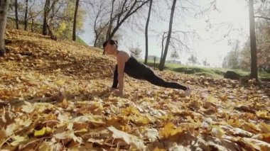 Sonbahar parkındaki fitness antrenmanından önce genç bayan antrenmanı. Sağlıklı genç bir kadın dışarıda ısınıyor. Ağır çekimde geniş açılı çekim. Sağlıklı bir yaşam tarzı. Kamera kaydırma