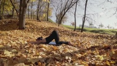 Sonbahar parkındaki fitness antrenmanından önce genç bayan antrenmanı. Sağlıklı genç bir kadın dışarıda ısınıyor ve omurgasını esnetiyor. Ağır çekimde geniş açılı çekim. Sağlıklı bir yaşam tarzı. Kamera kaydırma