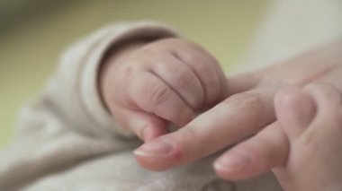 Bebeğin küçük elinin yavaş çekimde annenin sevgi dolu eline uzanarak çekilmiş yakın çekim. Parmağını tutarken elini okşuyor. Aşk ve aile kavramı.