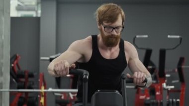 Spor salonunda fitness bisikleti güçlü redhead adam eğitim kardiyo egzersiz. Gözlüklü yetişkin sakallı adam yavaş çekimde sabit bisiklete biniyor.