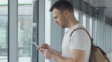 Adam havaalanında cep telefonu yakışıklı adam cep telefonu uçuş numarasını kontrol çanta ile cep telefonu kullanarak e-posta okuma uçak bekliyor. Copyspace ile akıllı telefon bakarak erkek orta çekim
