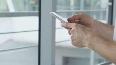 Havaalanı terminalinde cep telefonu kullanan ve uçağa binmeyi bekleyen bir adam. Telefon kullanarak erkek rezervasyonunun yakın çekim. Kopya alanı ile elinde cep telefonu tutan genç adam.