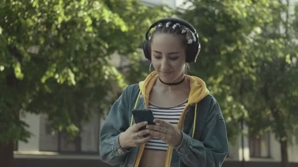 年轻女子用无线耳机和智能手机的按键屏来听音乐 千年使用智能手机和等待朋友 女性短信 — 图库视频影像