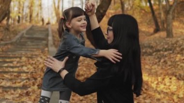Mutlu genç anne ve küçük kızı sonbahar parkında oynuyor, sarılıyor ve gülüyor. Aile mutluluğu. Orta atış