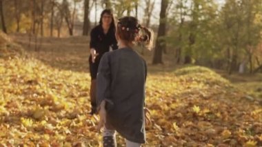 Anne elinde kızı nın etrafında dönüyor. Aile yavaş çekimde dışarıda eğleniyor. Kızı sonbahar parkında anneme koşuyor. Mutlu aile konsepti. Orta atış.